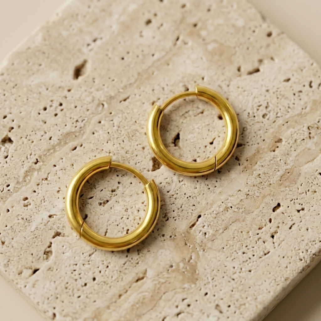 Gold little huggie hoop earrings displayed on a travertine block.