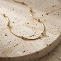 Celestial Bead Necklace draped across pale travertine, showing the spaced gold beads