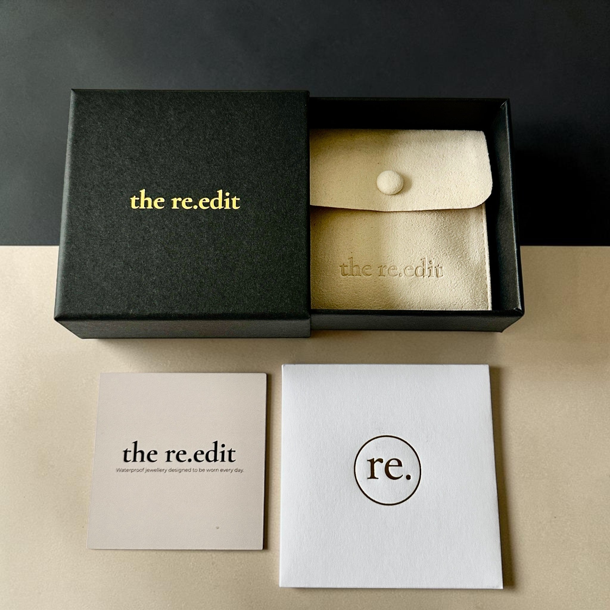 the re.edit jewellery packaging with black gift box, suede pouch and care cards on a dark background