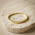 Meadow Hinged Bangle resting on pale travertine to show its smooth gold finish