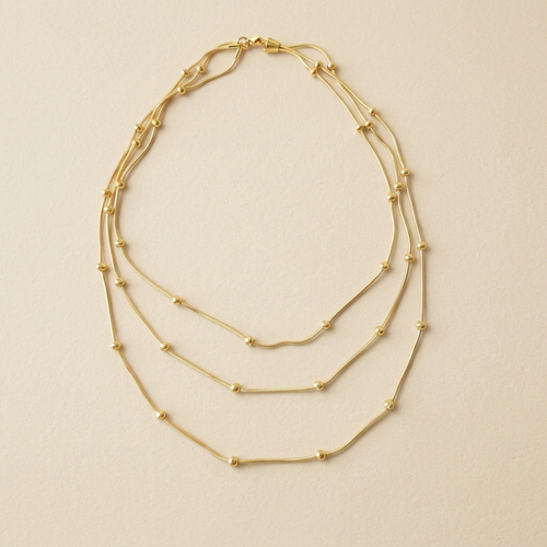Celestial Layered Necklace laid flat to show its three fine chains and gold bead details